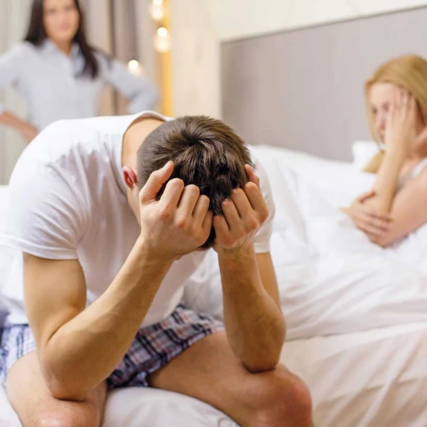 Man met handen in het haar op rand van het bed en op de achtergrond twee vrouwen - therapie bij ZEON
